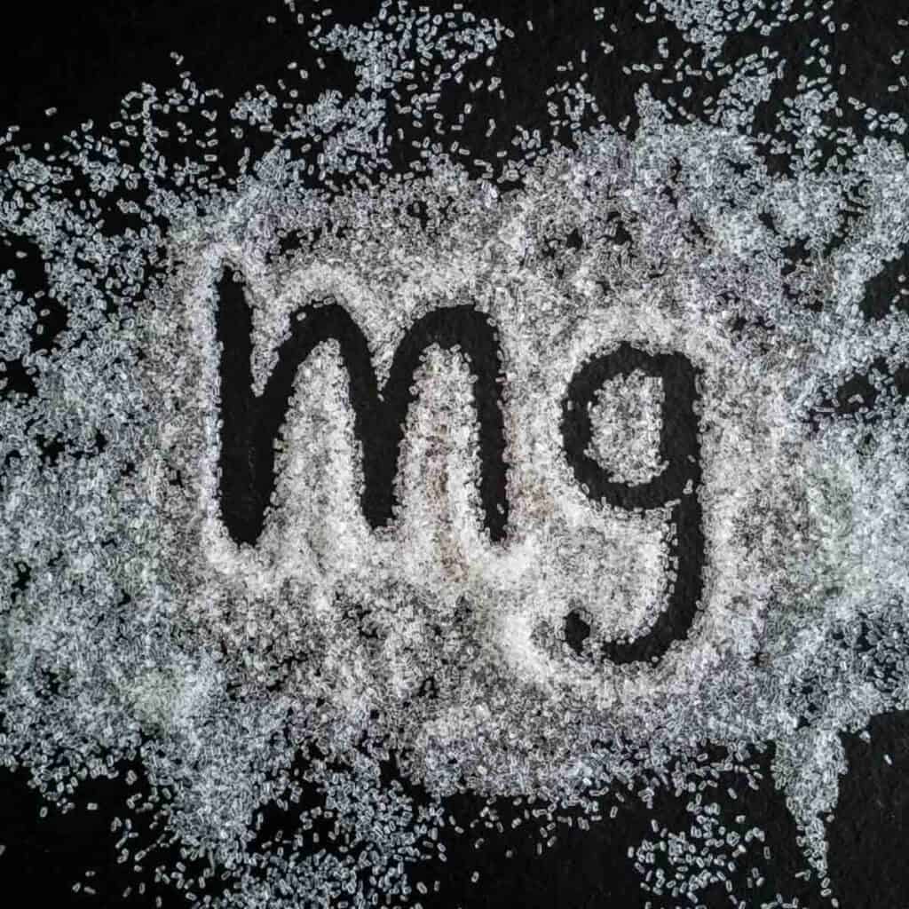 Abbreviation for magnesium written in a pile of white granules on a black background.