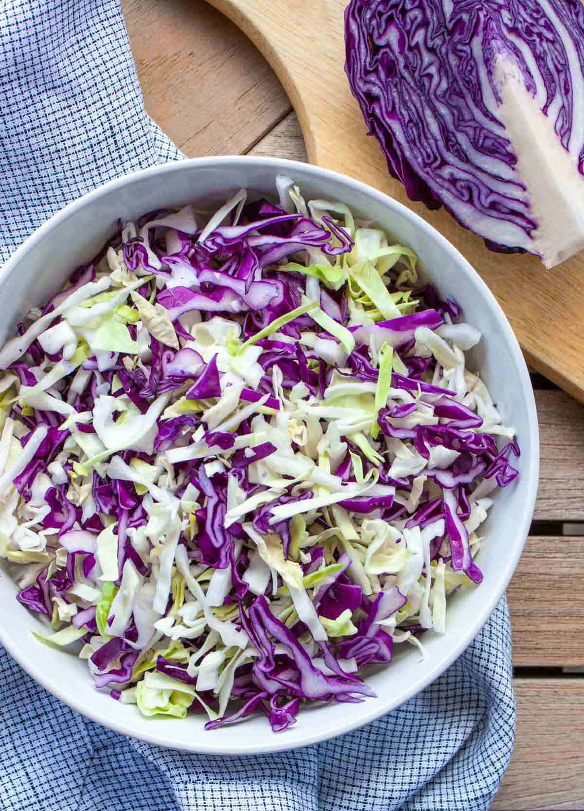 Shredded green and red cabbage in a white bowl on a checkered kitchen towel.