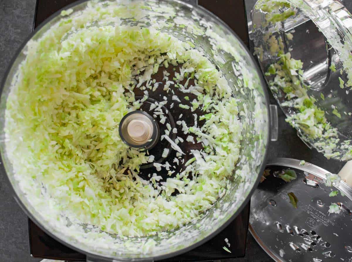 Shredded green cabbage in food processor bowl after using the grater attachment.