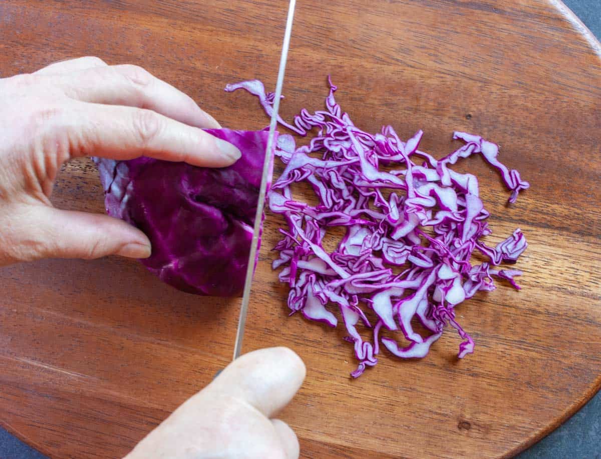 Slicing red cabbage quarter by hand into thin slices with a chefs knife.