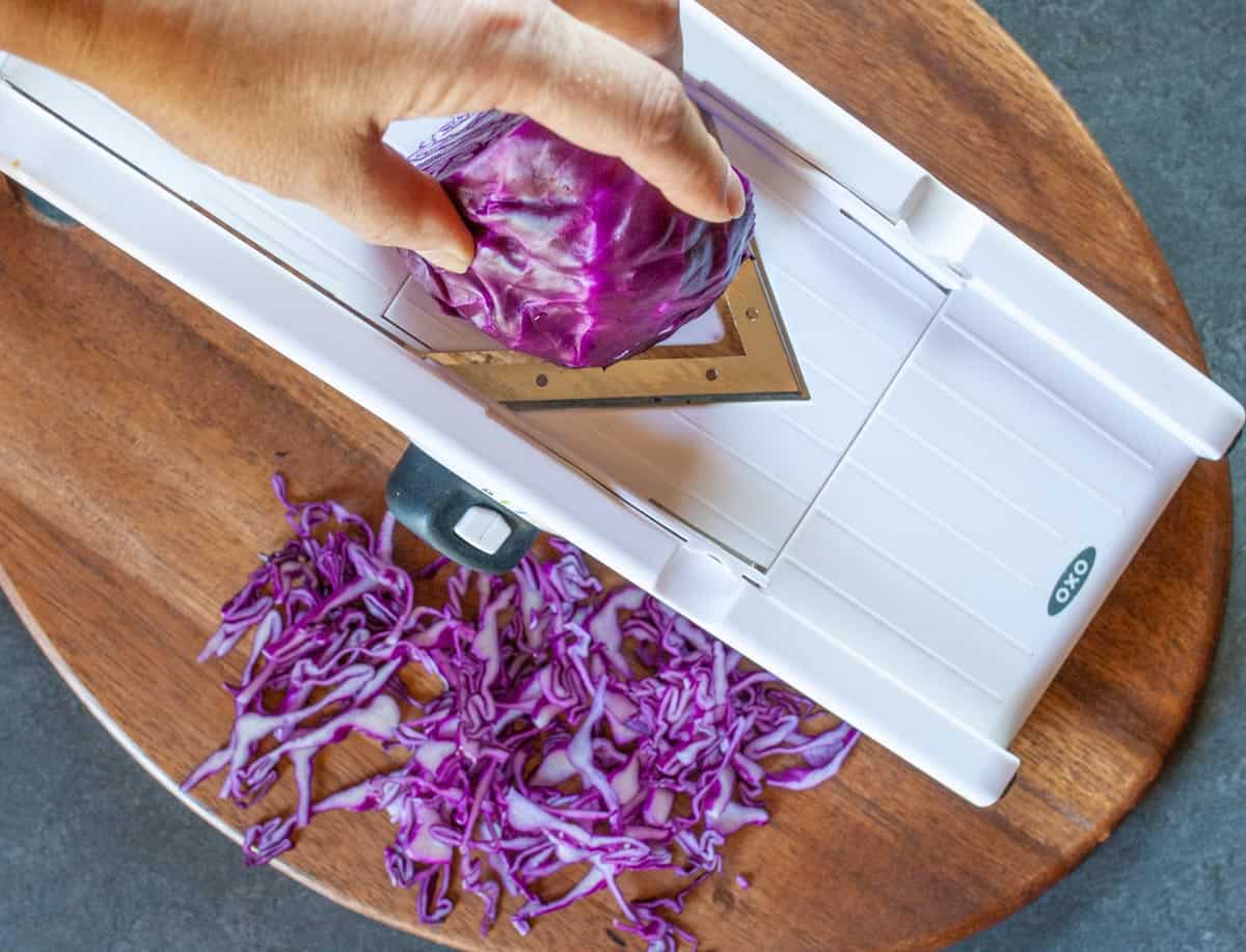 Slicing a red cabbage quarter head on a cutting board using a mandolin.