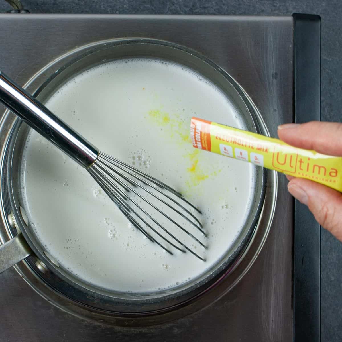 Adding packet of Ultima Replenisher to pan of coconut milk with whisk.