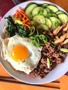 White plate of bibimbap with a sunny side up egg.