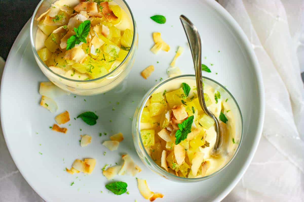 Two glasses of pineapple and lime topped panna cotta with a serving spoon.