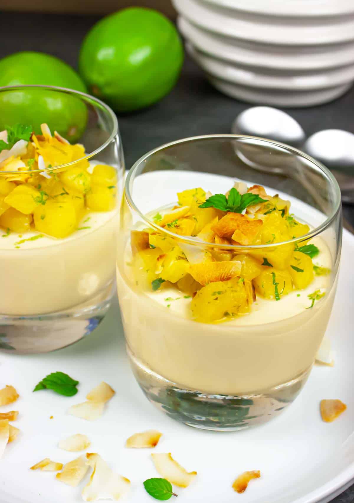 Two glasses of finished dessert topped with pineapple, toasted coconut flakes and mint.