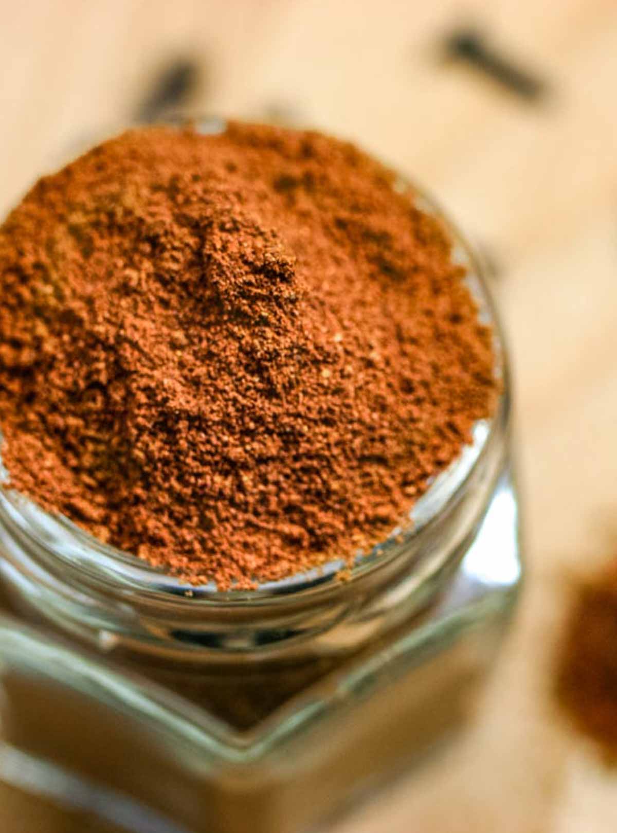 Spice jar overflowing with homemade pumpkin spice seasoning with a blurred backdrop.