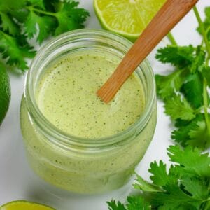Cilantro lime dressing in a wide mouth ball jar with a small wooden spoon in the jar.