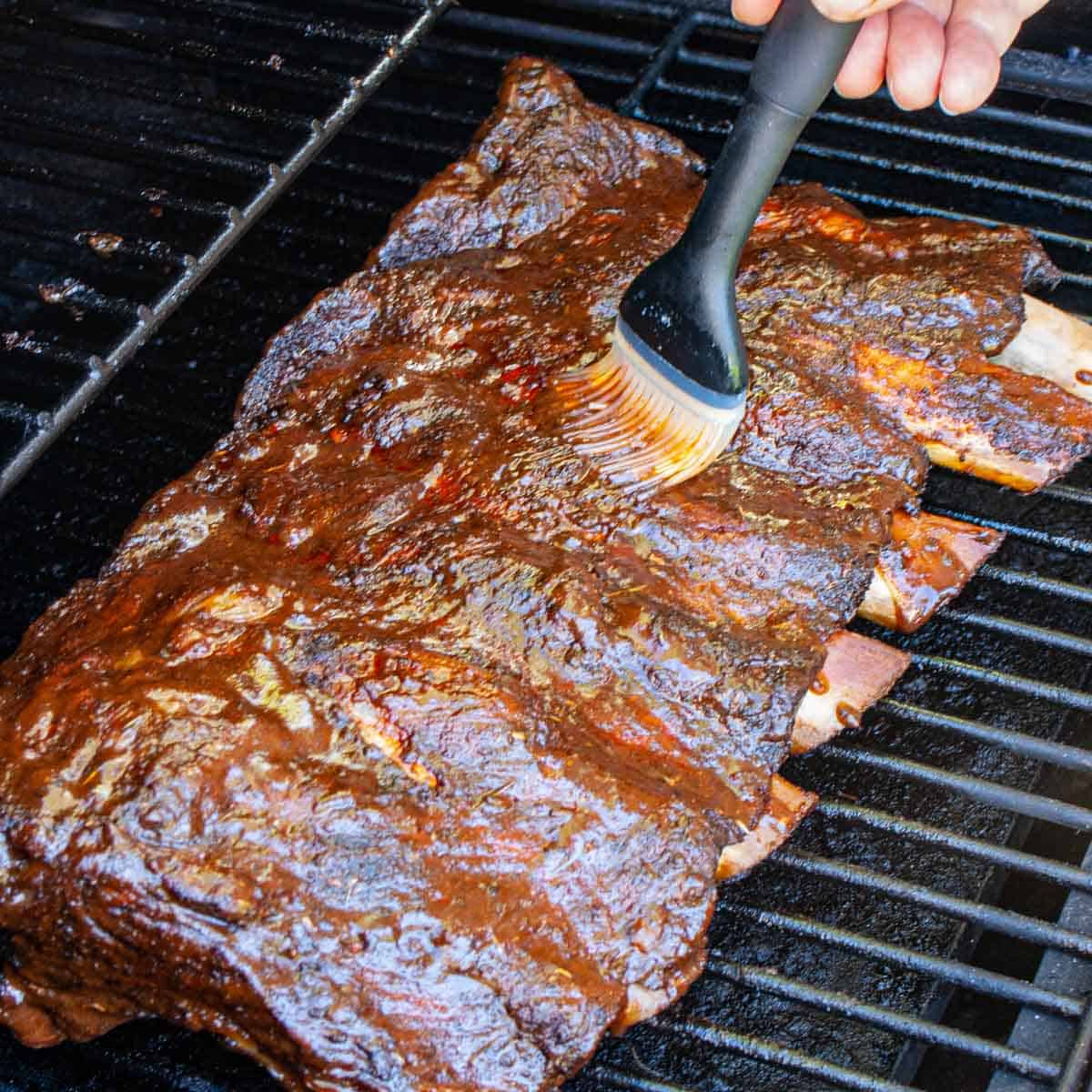 Applying sauce to a rack of beef ribs on the smoker.