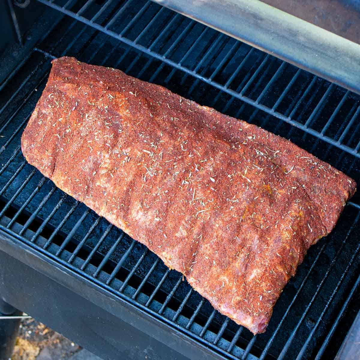 Rack of ribs freshly placed on smoker grill with caption.