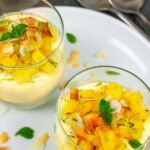 Two glasses of panna cotta topped with pineapple and coconut salsa and a mint leaf garnish.