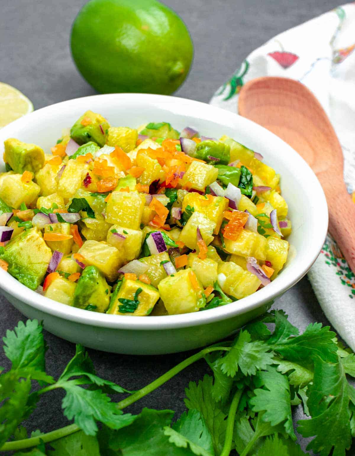 Pineapple salsa in white bowl with habanero on top and a cilantro garnish.