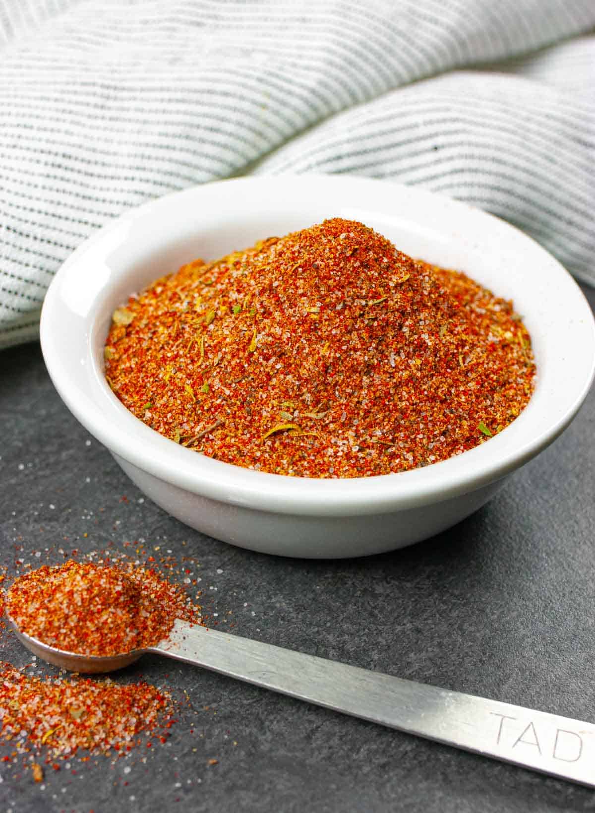 Small white bowl of keto seasoning for barbeque with a measuring spoon full on the side.