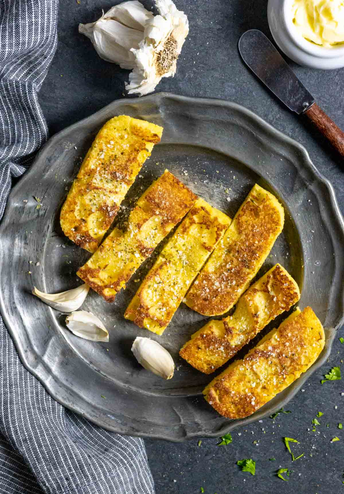 Pewter plate with six garlic parmesan oregano breadsticks with garlic cloves on the side.  Captioned with garlic bread instructions.