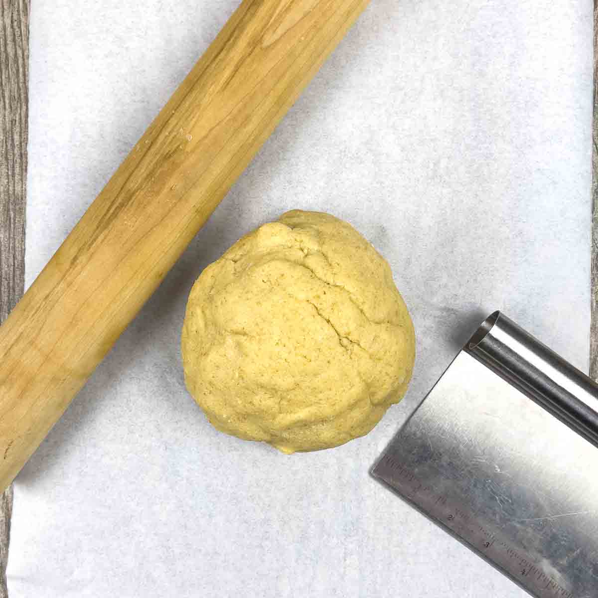 Ball of dough with a rolling pin and a pastry cutter on parchment paper.