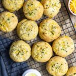 Cheddar biscuits cooling on a black rack with small cups of chives, cheese and butter on the side.