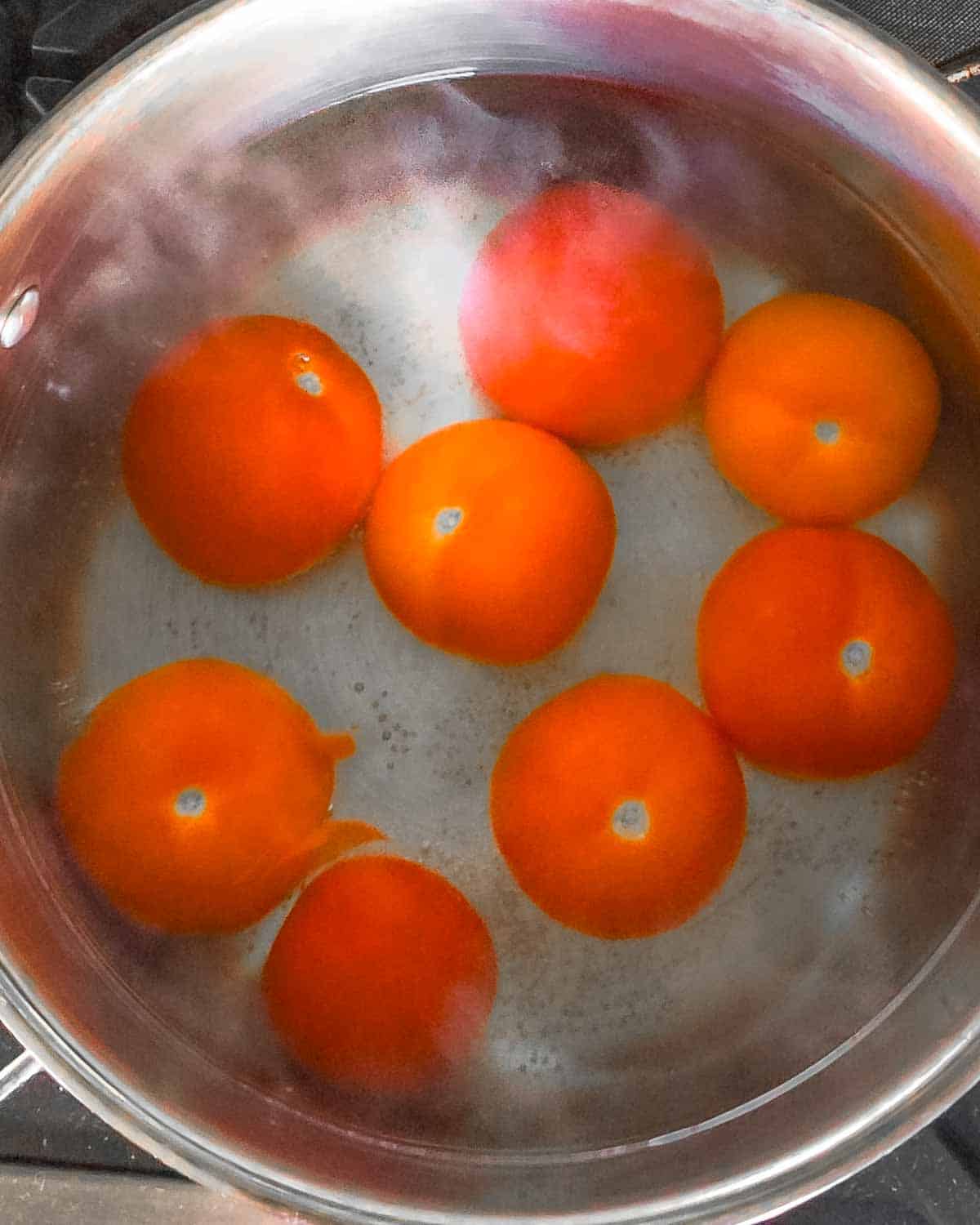 Red tomatoes being blanched and steaming in a large pot of hot water.