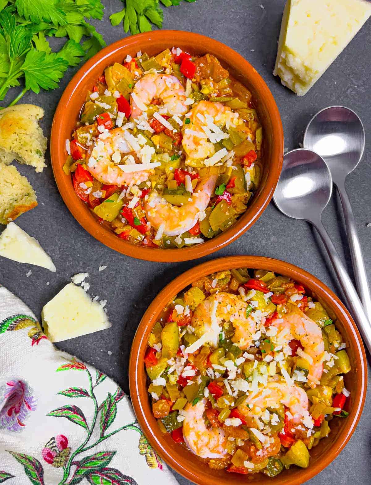 Two terra cotta cazuelas filled with Spanish vegetable stew topped with whole shrimp and manchego cheese.