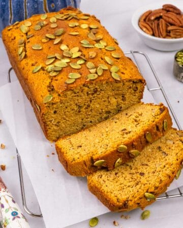Sliced gluten-free pumpkin bread topped with pumplin seeds on a rack with a decorative knife.