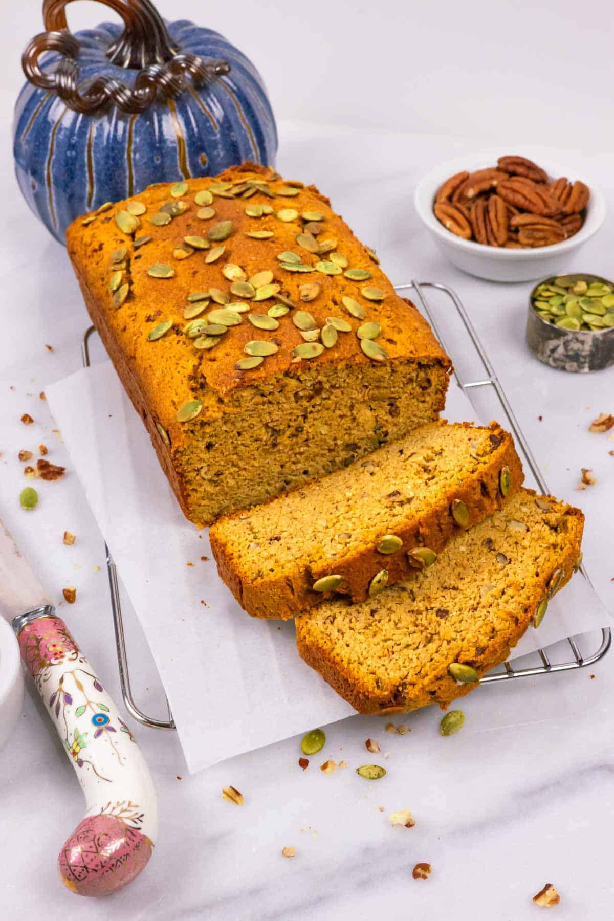 Baked loaf of pumpkin bread topped with pumpkin seeds with two slices laying in front.