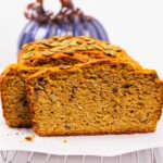 Sliced loaf of pumpkin bread showing texture of slice with nuts and golden moistness.