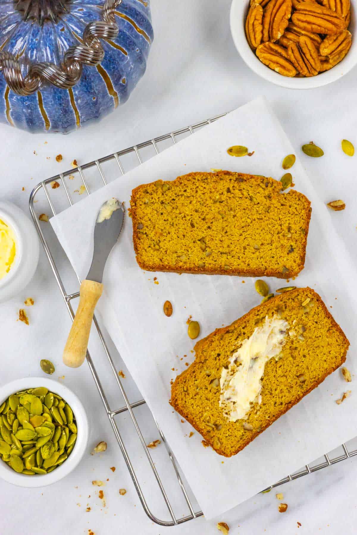Two slices of low fodmap pumpkin bread on a cooling rack with butter spread on one slice.
