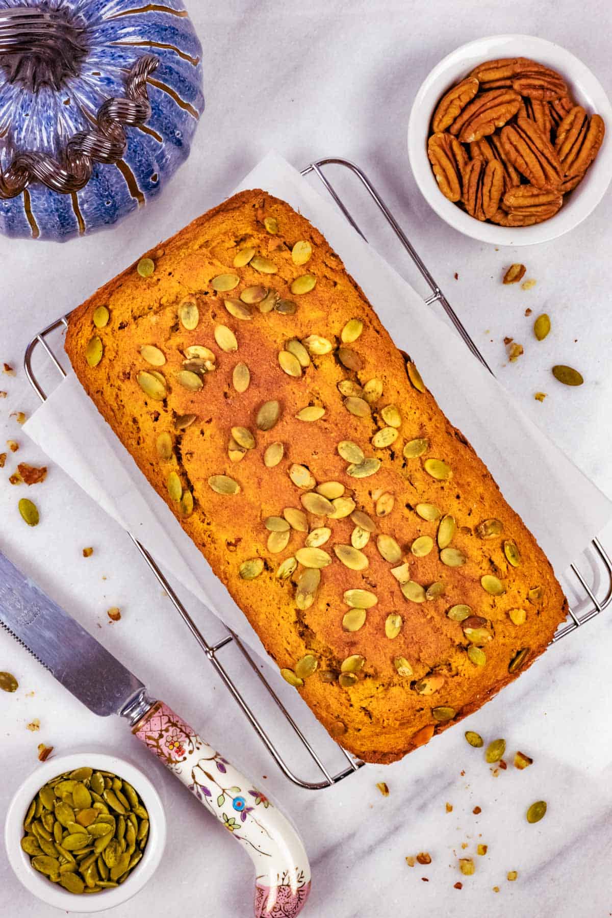 Golden baked whole loaf of keto pumpkin bread on a cooling rack with a  fancy handled knife and seeds.