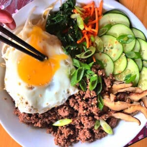 Keto bibimbap bowl with veggies, and an egg on top with chopsticks poking the yolk.