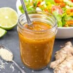 Jar of golden sesame dressing with whisk inside, and whole ginger on the side.