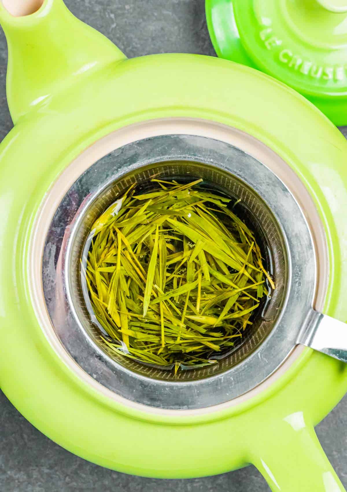 Green tea pot with steel basket of bamboo tea steeping in the pot.