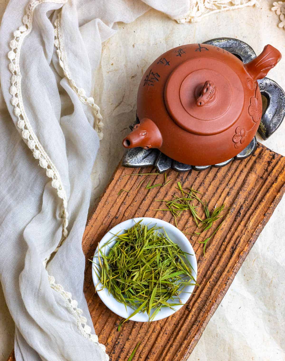 Clay pot on a trivet on a clay board with a white bowl of loose tea leaves.