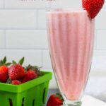 Tall shake glass with strawberry smoothie, basket of berries and one on the rim.