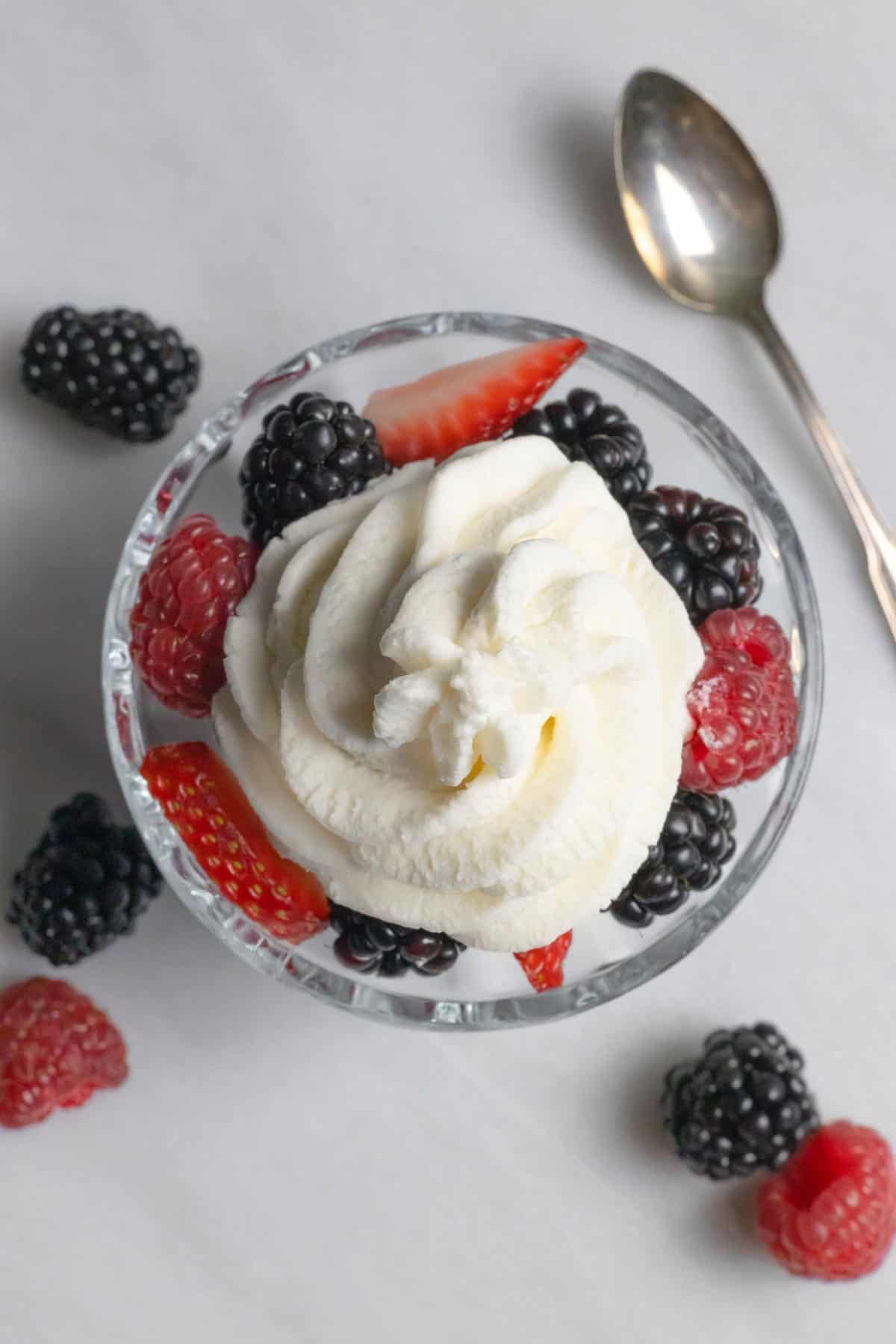 Dessert dish with raspberries, sliced strawberries and blackberries topped with piped sugar-free whipped cream.