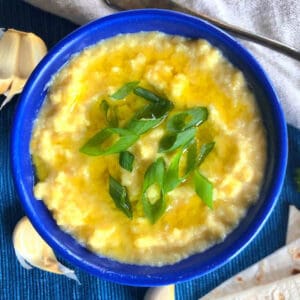 Blue bowl of greek skordalia topped with olive oil and sliced green onion tops for garnish.