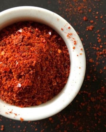 Offset image of colorful orange-red Aleppo pepper ground and in a small white bowl.