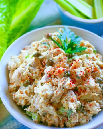 Chicken artichoke salad with jalapenos in a small white bowl with capers and parsley garnish.