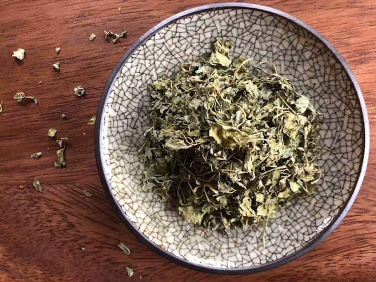 Dried fenugreek leaves on a small decorative plate with cracked design on a wood surface.