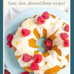 Fully decorated lemon raspberry bundt cake on a blue cake pedestal topped with low carb icing and whole raspberries.