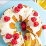 Lemon raspberry bundt cake on a blue cake pedestal topped with lemon glaze and whole raspberries.