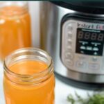 Open quart jars of chicken broth in front of an Instant Pot with herbs sprinkled in front.