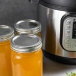 Three lidded quart jars of chicken bone broth next to an Instant pot with a small bunch of orange carrots with tops in front.