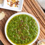 White bowl of Mexican chimichurri sprinkled with Aleppo pepper on a clay textured plate.