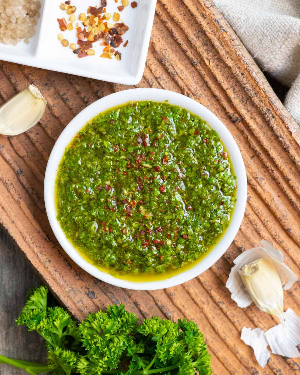 White bowl of Mexican chimichurri sprinkled with Aleppo pepper on a clay textured plate.