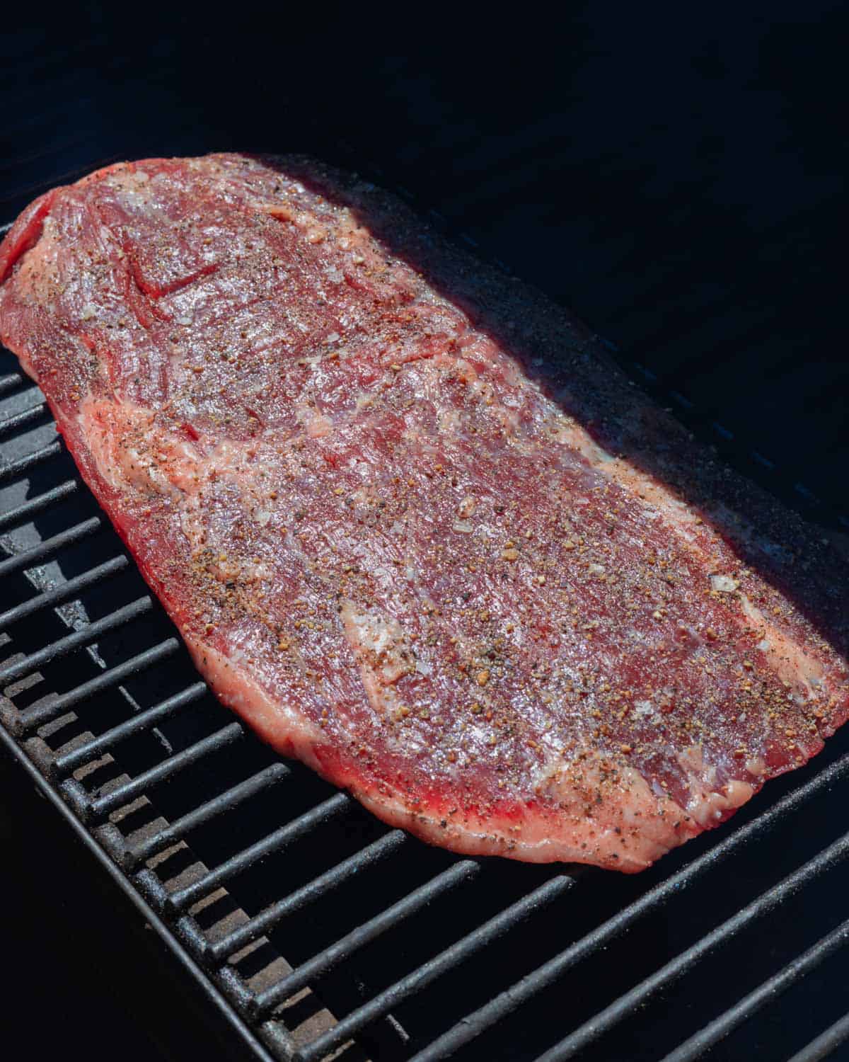 Flank steak, seasoned and placed on the smoker grill grates.