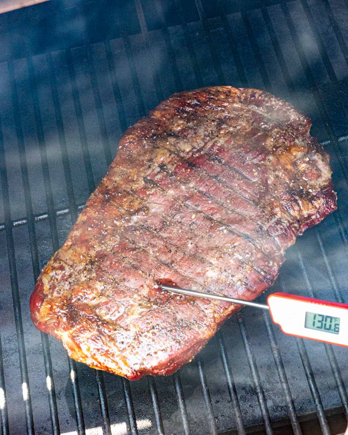 Instant read thermometer poked in seared flank on the smoker to test level of doneness.