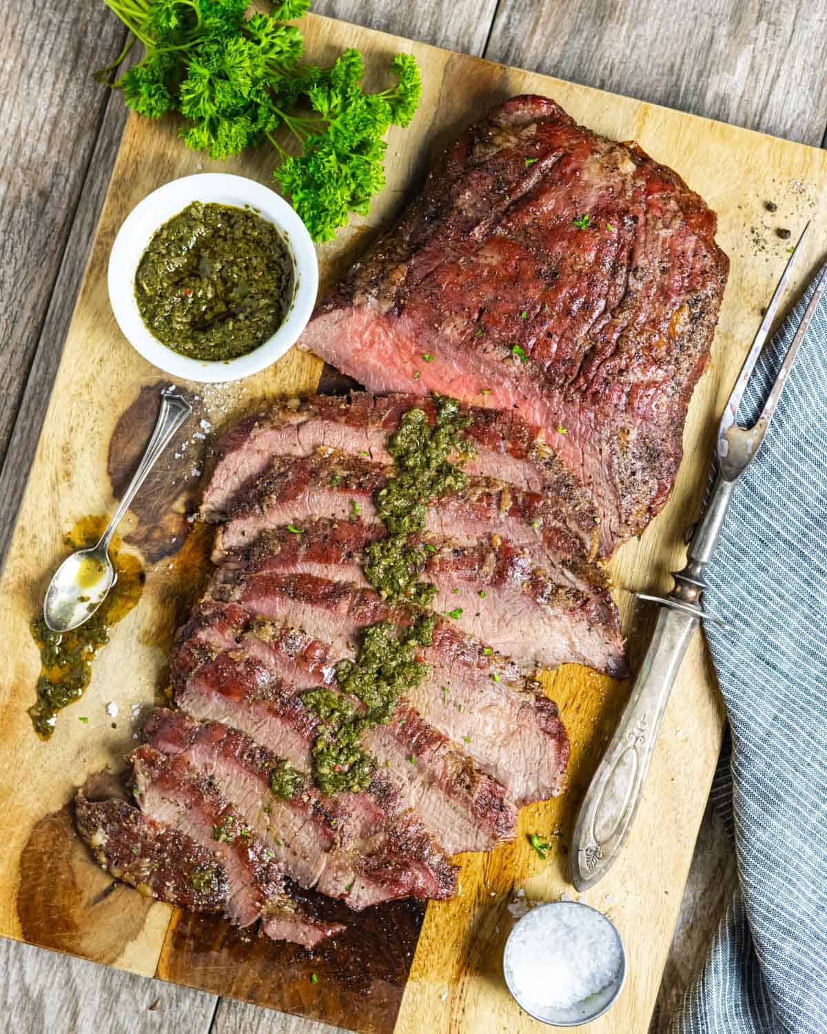 Smoked flank steak cut in layered thin slices on a board with Mexican chimichurri sauce spread down the center.