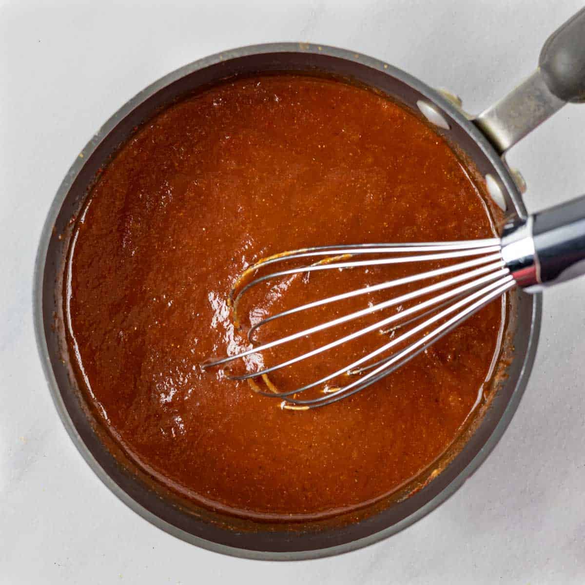 Saucepan of mixed BBQ sauce ingredients with a whisk.