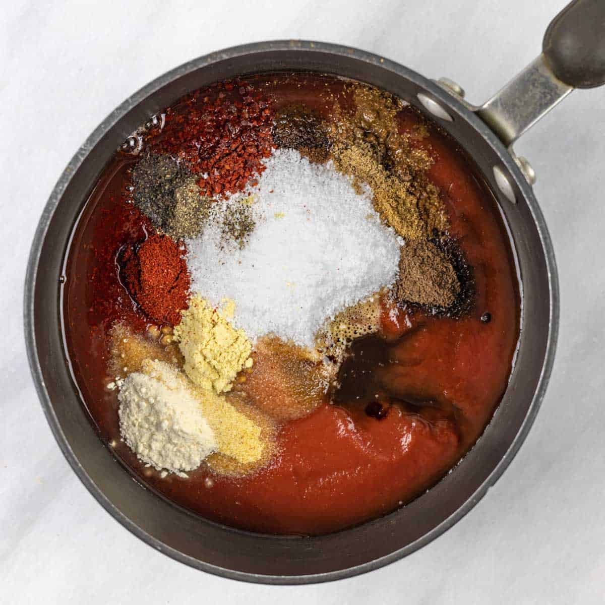 Tomato sauce and powdered ingredients in piles in a saucepan ready to stir and simmer.