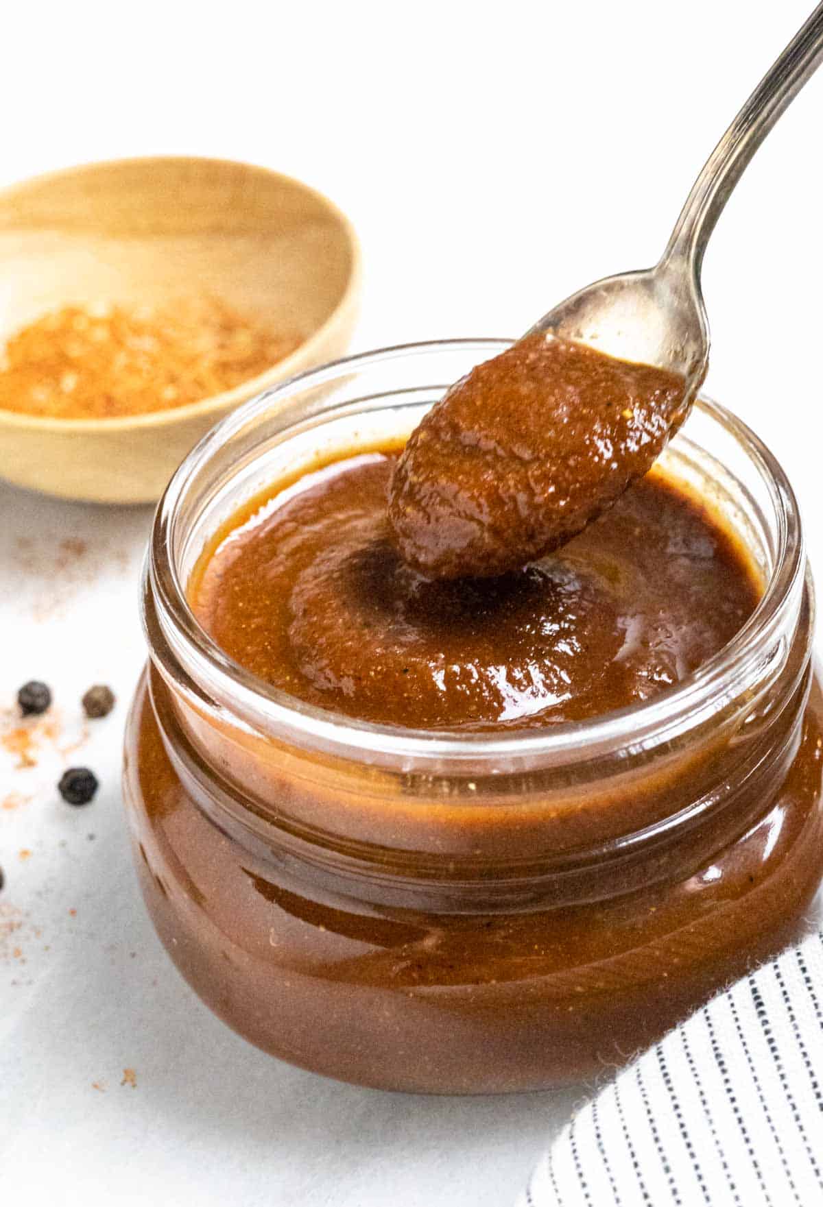 Low-FODMAP barbeque sauce in a glass jar with a scoop on a spoon pouring back into the jar.