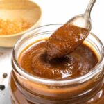 Low-fodmap barbecue sauce in a glass jar with a scoop on a spoon pouring back into the jar.