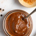 Jar of rich, red, low fodmap barbecue sauce next to a small wood bowl of spices.